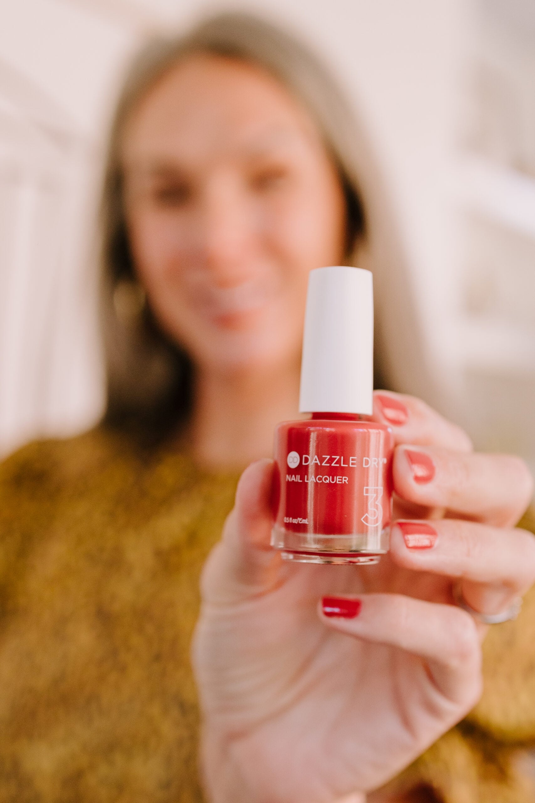 A smiling woman holding up a bottle of red nail polish.