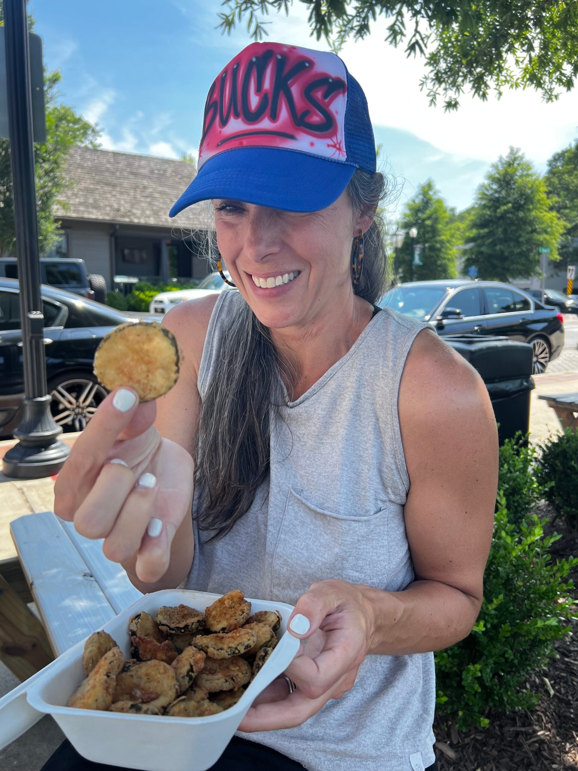A woman eats fried pickles while smiling.
