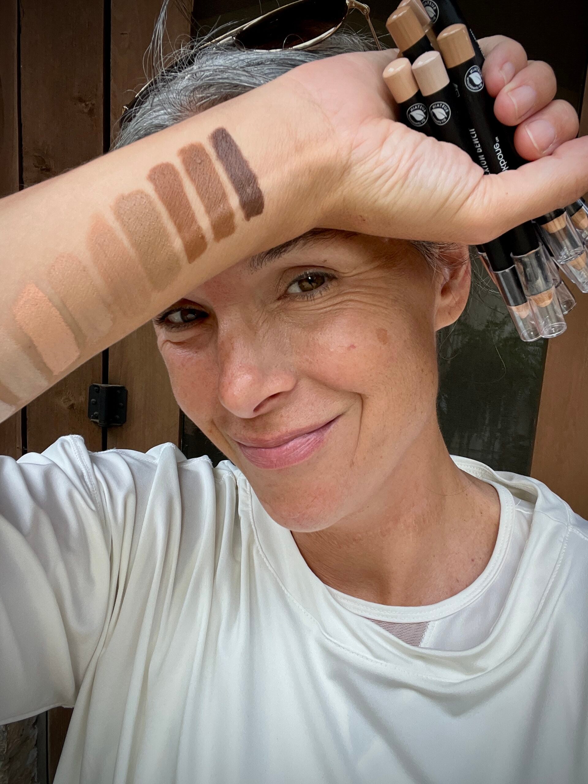 A smiling woman with a number of swatches of concealers on her wrist and forearm.